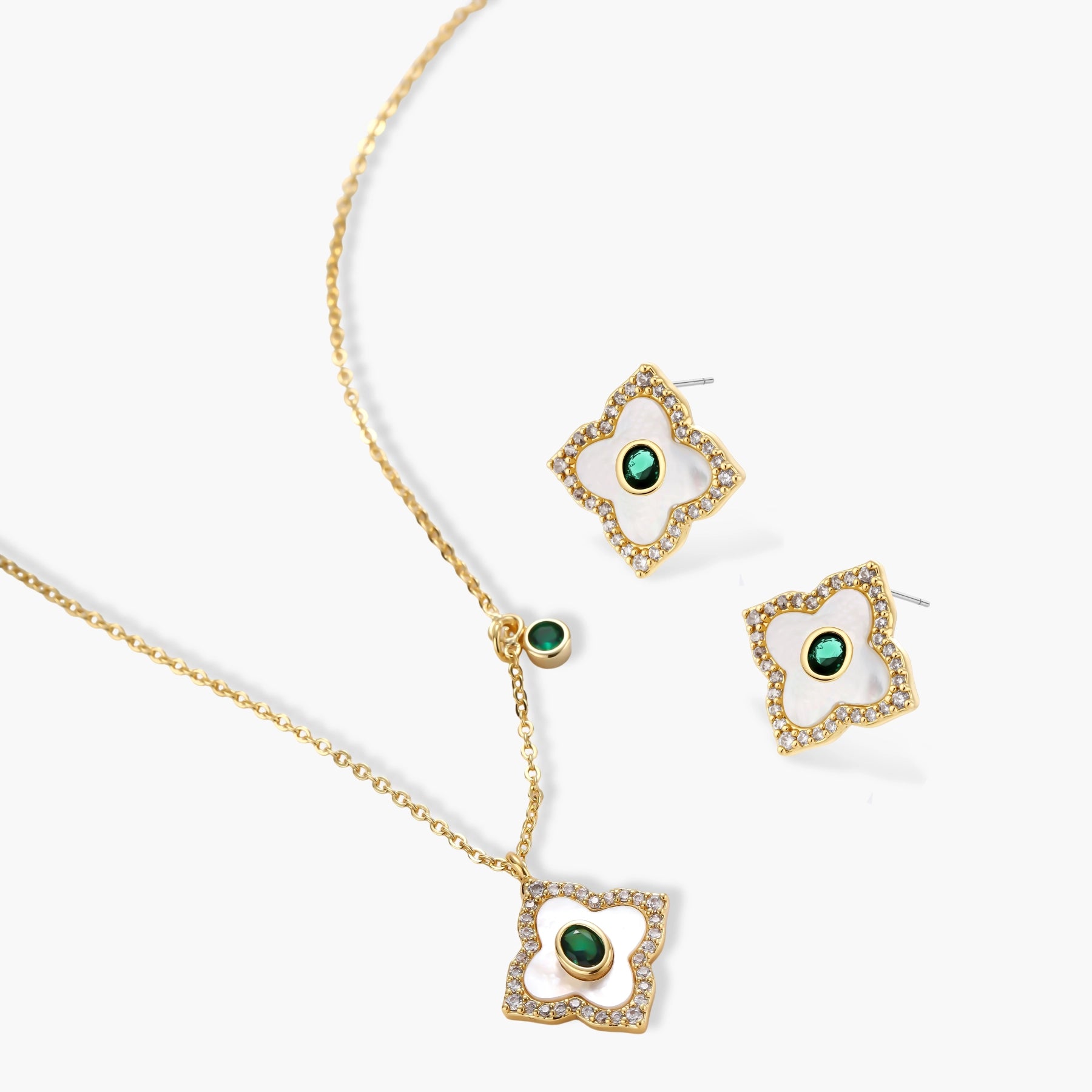 Gold-plated quatrefoil pendant and earrings with white enamel, emerald CZ center stones, and crystal borders on white background.