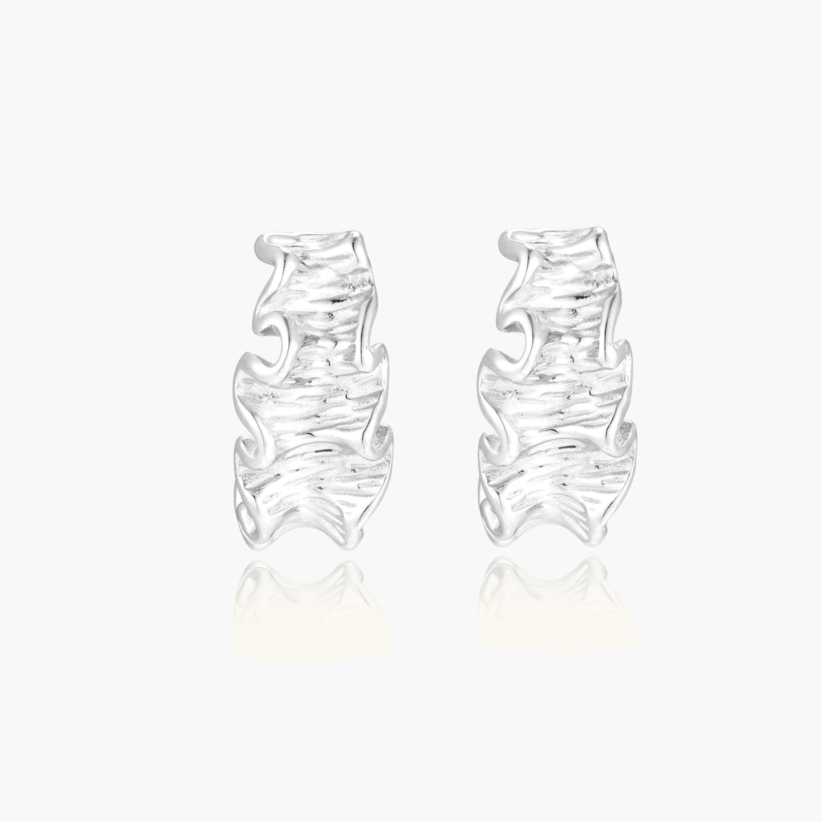 White gold plated sculptural hoop earrings with organic wavy edges and reflective metallic finish on cream background