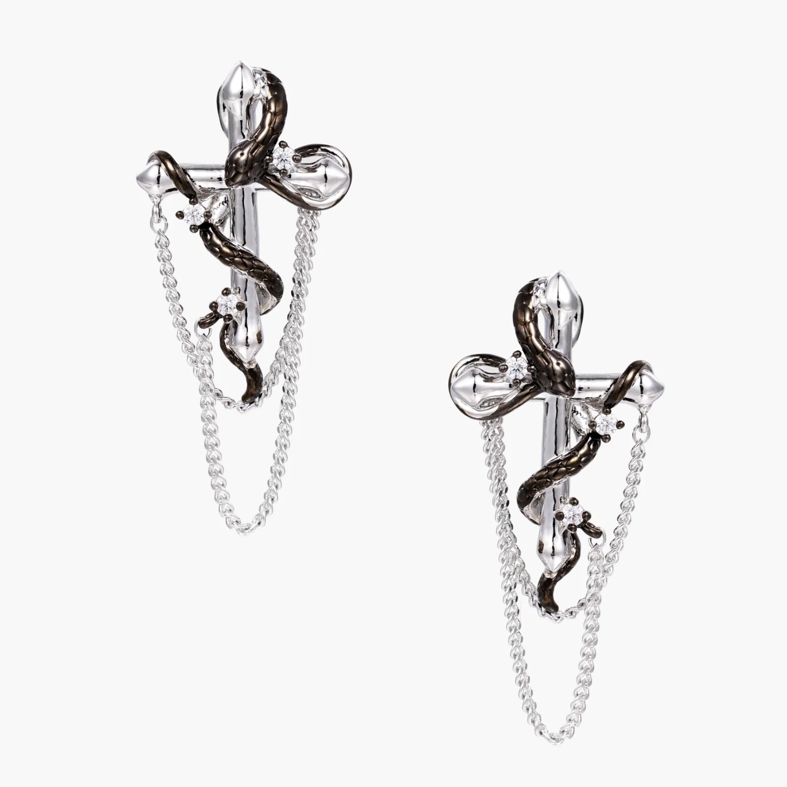 Silver dangle earrings with sculptural serpent coiled around cross shape and delicate chain accents on cream background
