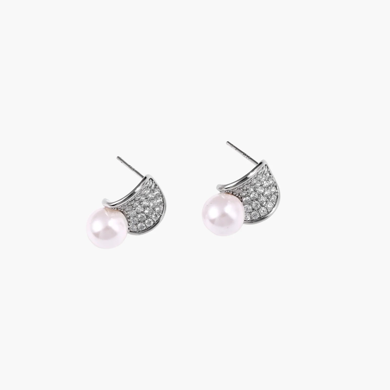 Curved pavé diamond studs in white gold-plated brass cradle lustrous freshwater pearls against cream background