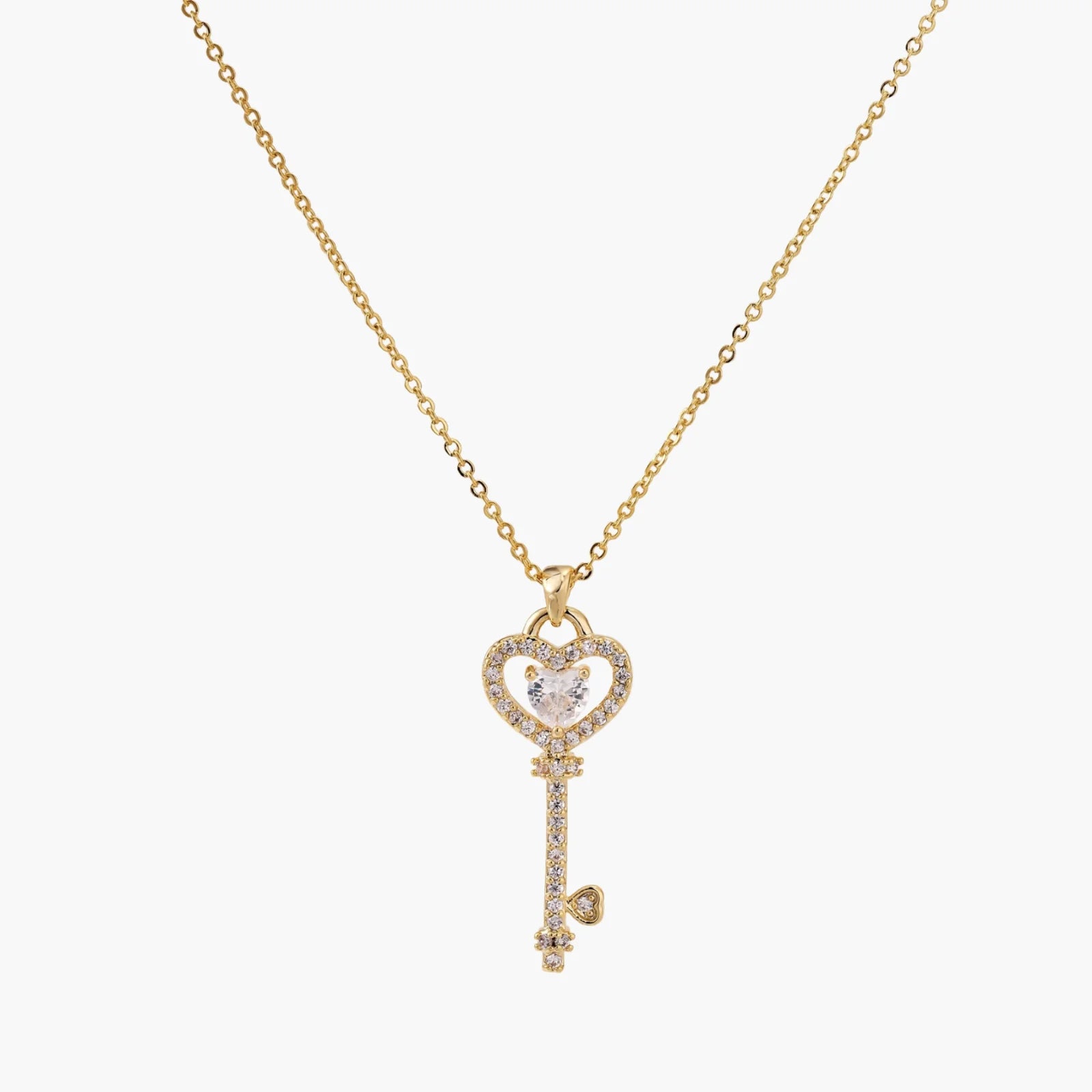 Delicate gold key pendant with heart-shaped bow and crystal pavé detailing on fine chain against cream background.