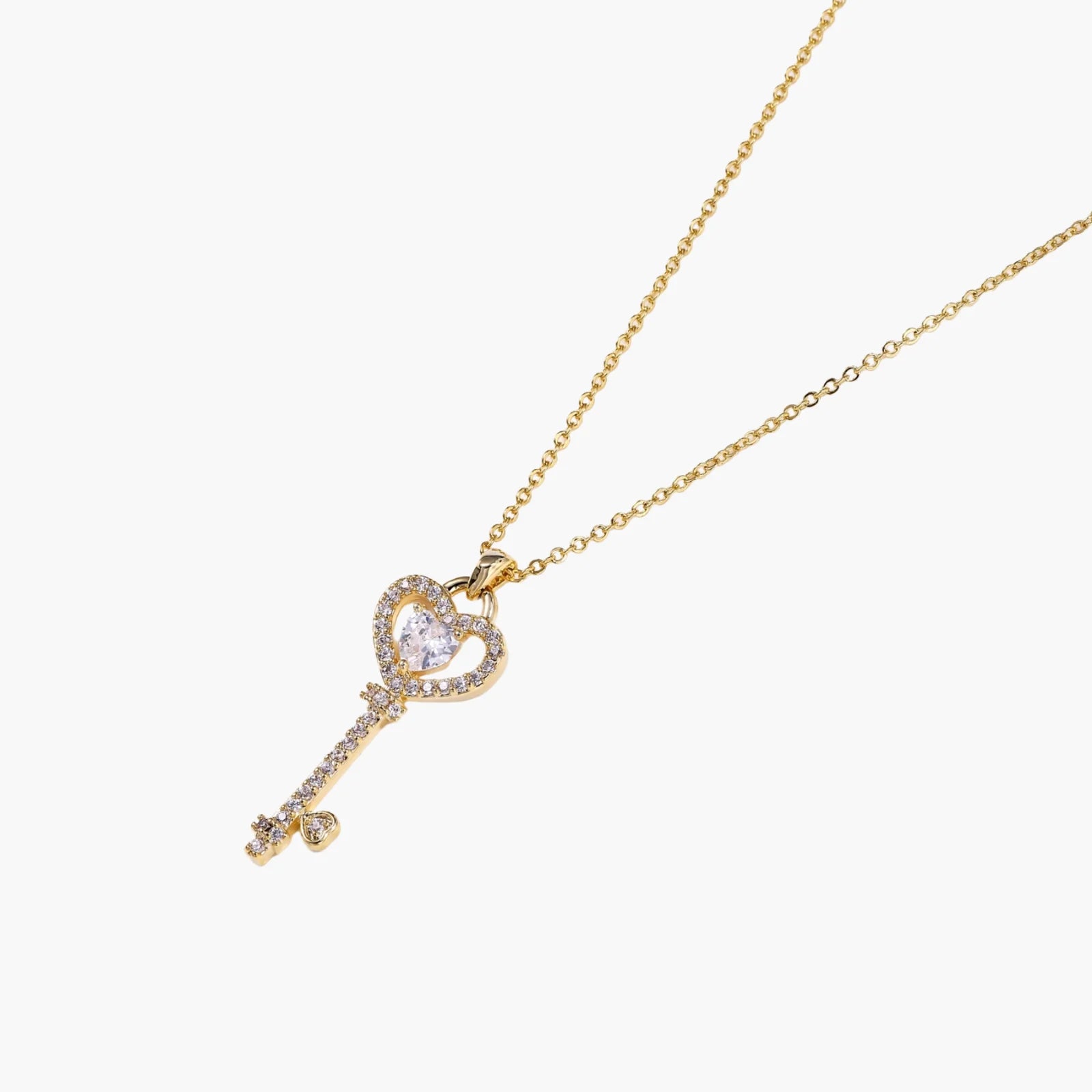 Delicate gold key pendant with heart-shaped bow and crystal pavé detailing on fine chain against cream background.