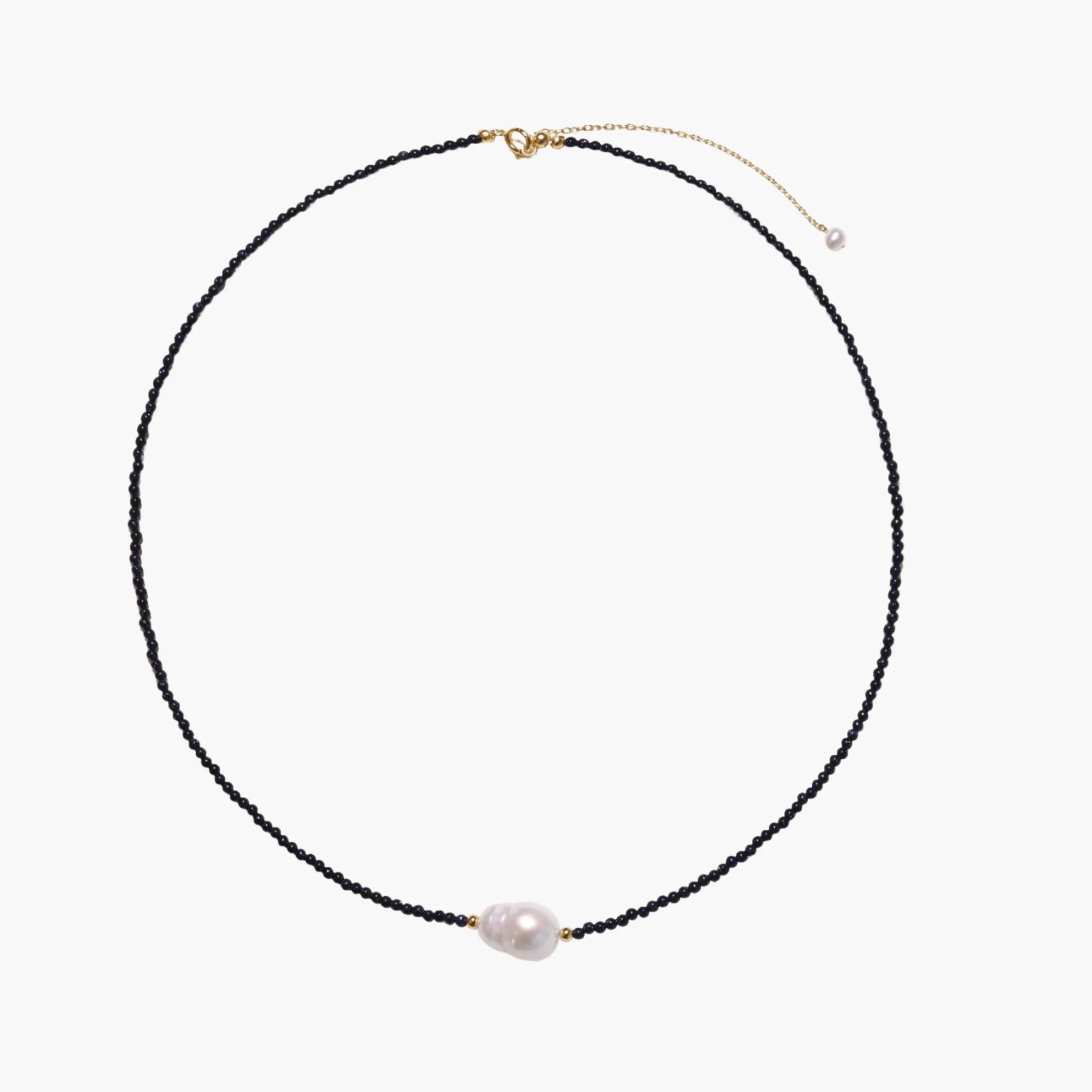 Delicate necklace with black blue sandstone beads and baroque pearl center on white background with gold accents.