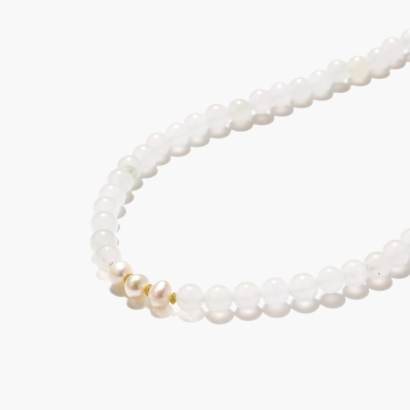 Three layered white beaded bracelets with carved orange agate lotus centerpiece and freshwater pearls on cream background.