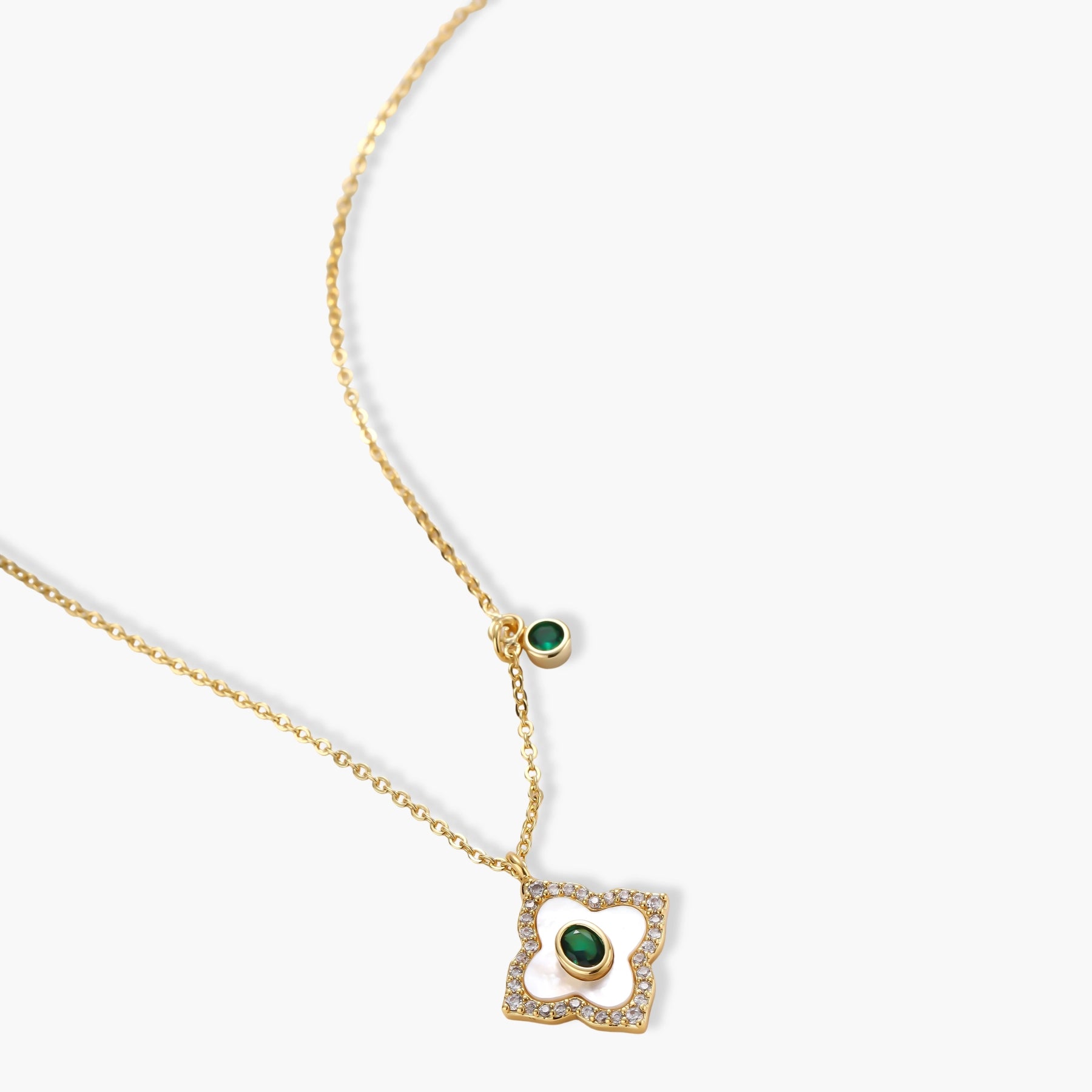 Gold-plated quatrefoil pendant and earrings with white enamel, emerald CZ center stones, and crystal borders on white background.