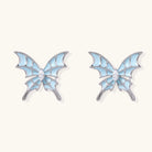 Long silver-tone earrings with powder blue enamel butterfly studs and flowing chain tassels on cream background