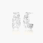 White gold plated sculptural hoop earrings with organic wavy edges and reflective metallic finish on cream background