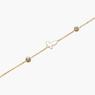 Gold chain bracelet with white mother of pearl butterfly pendant and two bezel-set crystals on cream background