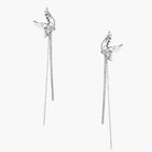 Pair of silver wing-shaped earrings with feather details and long sparkling crystal chain drops on cream background