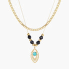Layered gold necklace with turquoise evil eye pendant and black quartz beads on cream background
