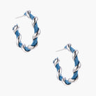 White gold-plated hoops intertwined with blue denim fabric in a twisted rope design on cream background.