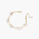 Double-strand gold bracelet with irregular baroque pearls and smooth freshwater pearls on cream background.