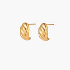 Chunky gold twisted rope huggie hoops with diagonal grooves and high-polish finish on cream background