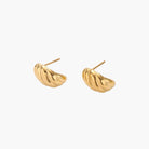 Chunky gold twisted rope huggie hoops with diagonal grooves and high-polish finish on cream background
