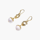 Gold sunburst charm earrings with baroque pearl drops on French hooks against cream background