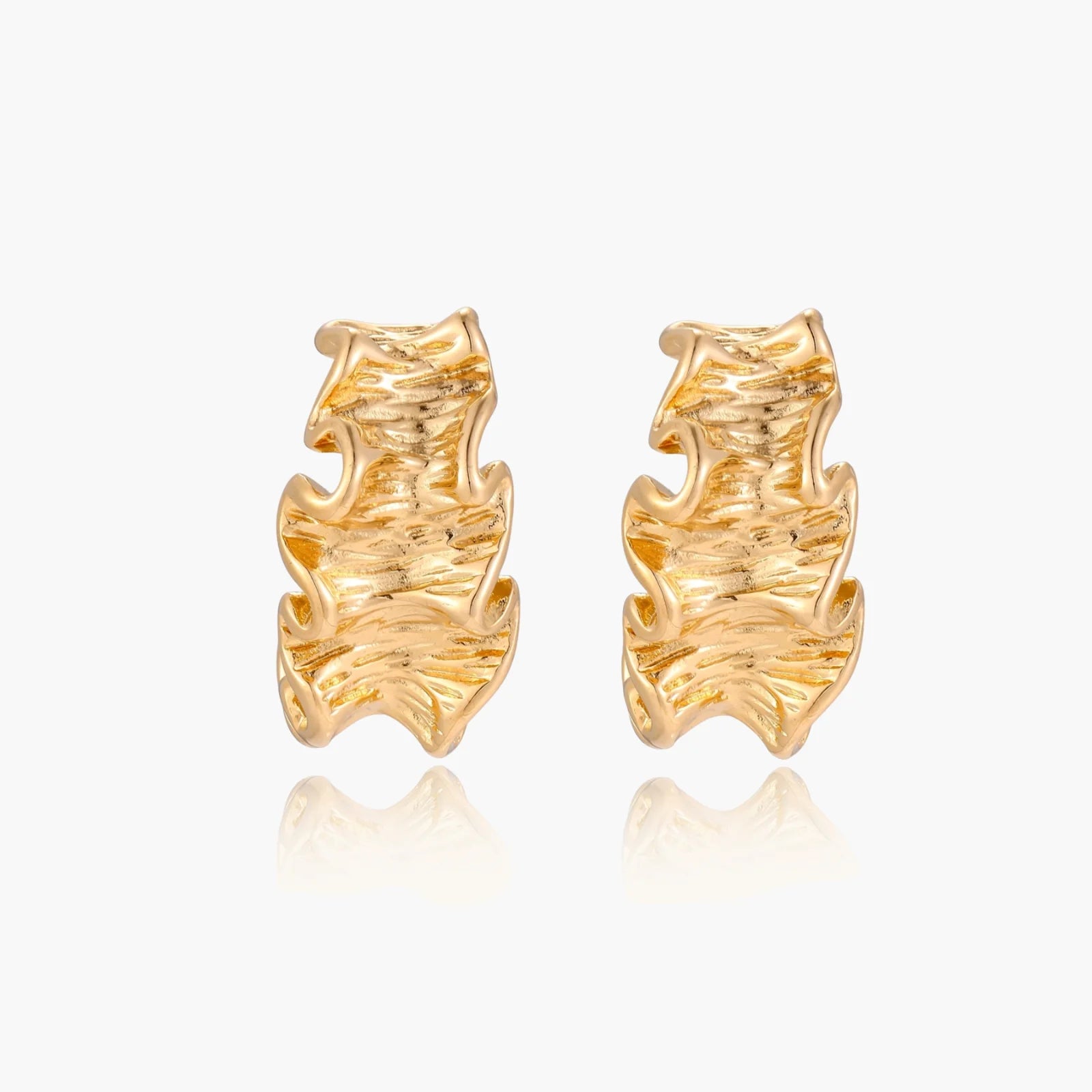 Pair of gold huggie hoops with sculpted wave texture and dimensional ripples on neutral background.
