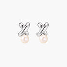 Rhodium-plated silver earrings with twisted X design and freshwater pearl drops on beige background