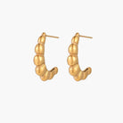 Gold-plated sculptural hoop earrings with chunky segmented design on cream background