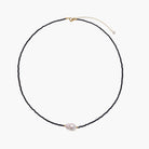Delicate necklace with black blue sandstone beads and baroque pearl center on white background with gold accents.
