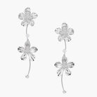 Silver-white asymmetric earrings with textured flower petals and crystal centers on cream background