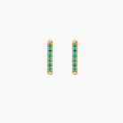 Pair of small gold huggie hoop earrings with bright green cubic zirconia stones on cream background