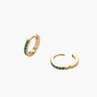 Pair of small gold huggie hoop earrings with bright green cubic zirconia stones on cream background