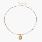 Delicate gold-plated necklace with mixed gemstone beads and ornate oval pendant on white background