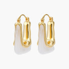 Sculptural gold-plated hoop earrings with flowing curved design and lever-back closure on cream background.