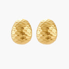 Pair of textured gold-plated sterling silver huggie earrings with dimpled surface finish on cream background.