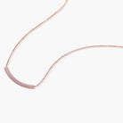 Rose gold jewelry set with pavé cubic zirconia stones including curved necklace, hoop earrings, and adjustable ring on cream background.